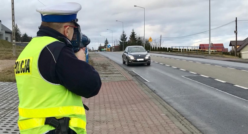 Policjant ruchu drogowego trzymając w ręku ręczny miernik prędkości mierzy prędkość jadącego po jezdni pojazdu / fot. KWP w Krakowie